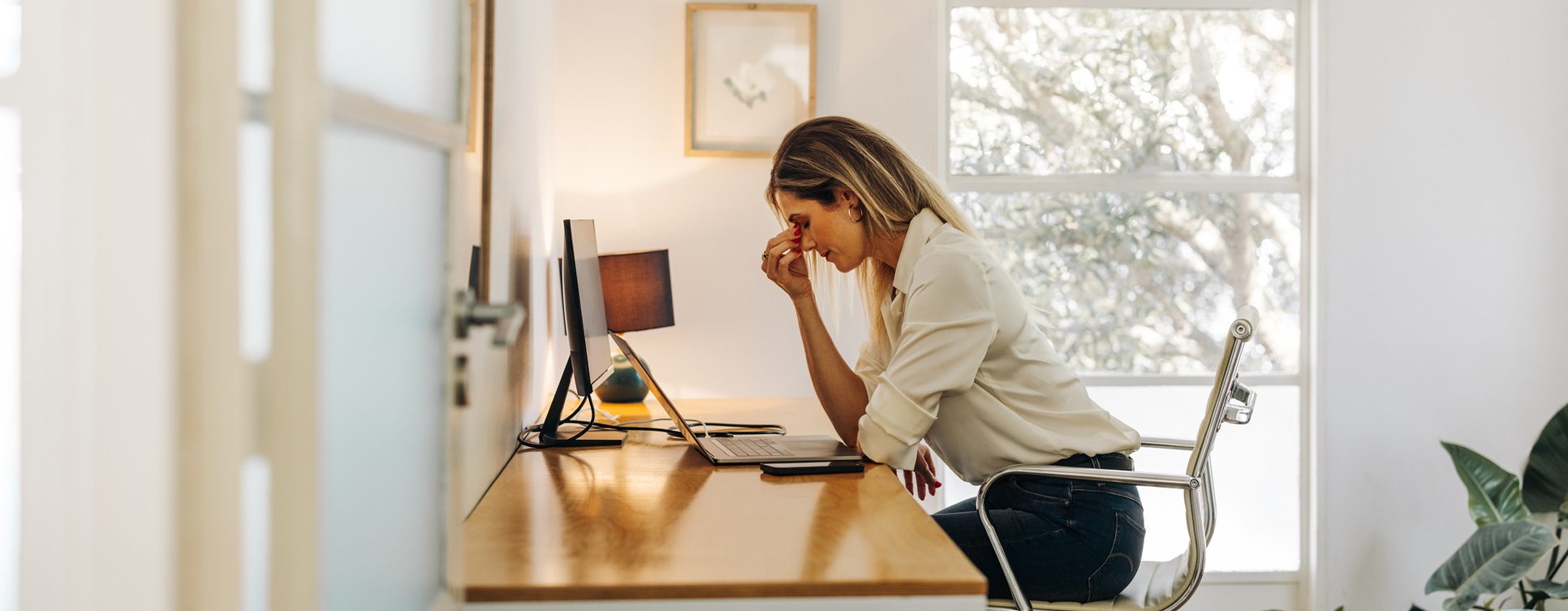 Exhausted businesswoman having a headache in her office. Overworked businesswoman experiencing work fatigue while siting in front of a laptop.